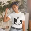 A woman with plants in the background wearing a white shirt with a manga design of an anime boy sitting