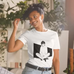 A woman with plants in the background wearing a white shirt with a manga design of an anime boy sitting