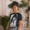 A woman with plants in the background wearing a black shirt with a manga design of a long hair anime girl